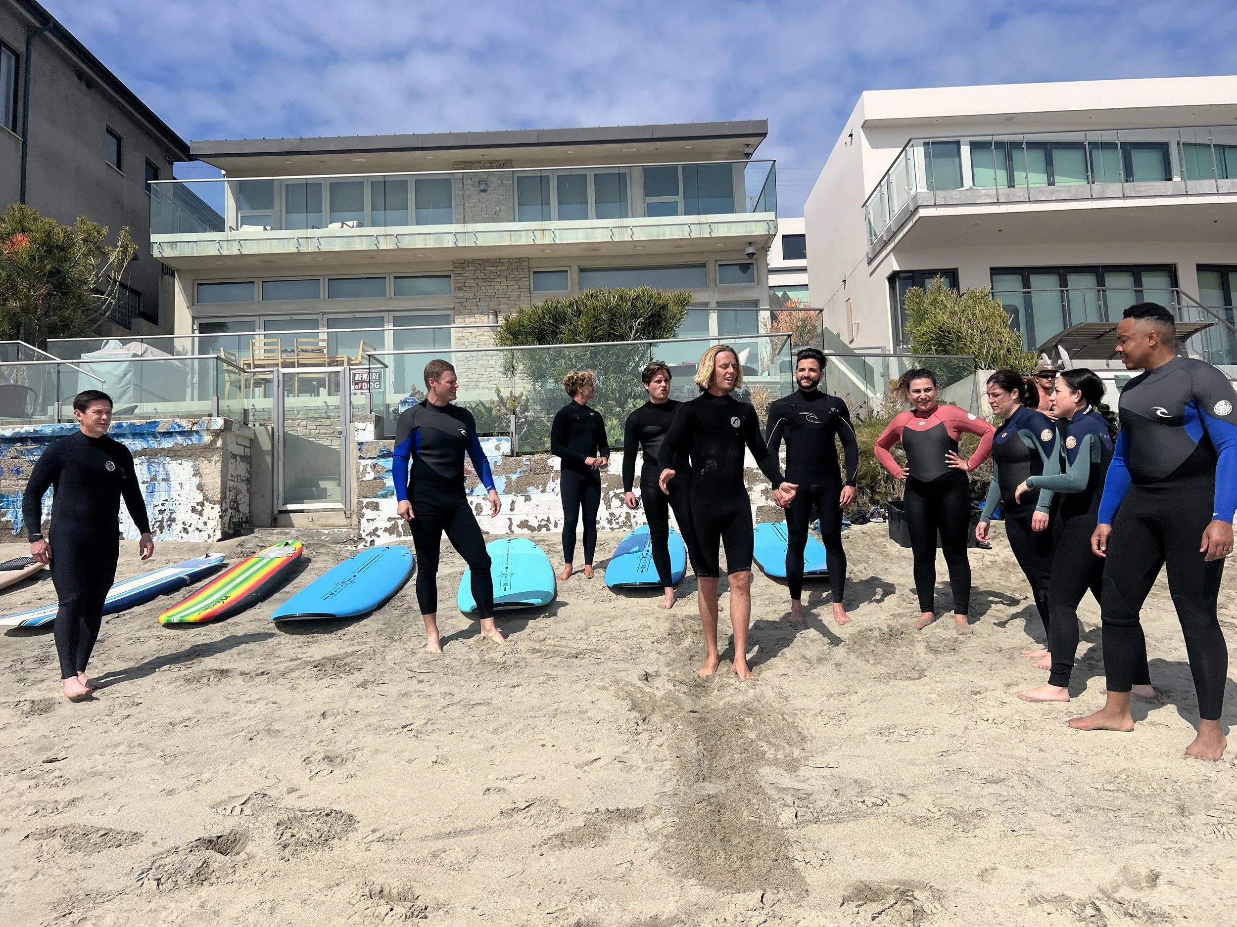 Team surf class in wetsuits with boards in front of Laguna Beach houses