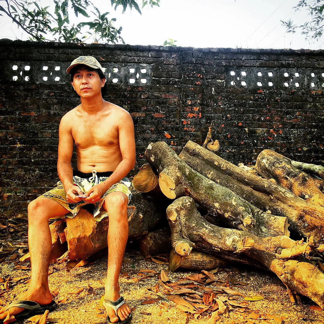 Kyaw Myoe Naung sits on Thanaka logs ready for processing at the factory. He is the grandson of this Thanaka company's founder in Mawlamyine, the capital city of Mon State.