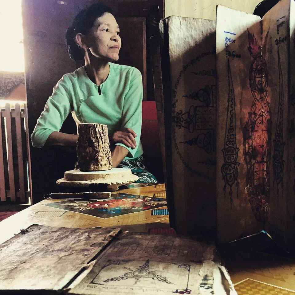 Daw Khin Aye sits in the company of her Thanaka log and grinder along with her husband's century-old traditional tattooing books passed down from his grandfather .