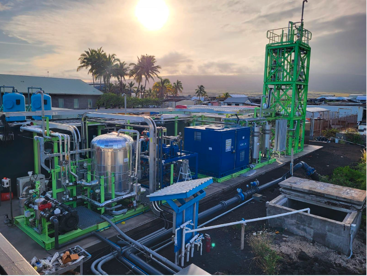 Industrial equipment with pipes, tanks, and machinery on a rooftop with palm trees and a sunset in the background.
