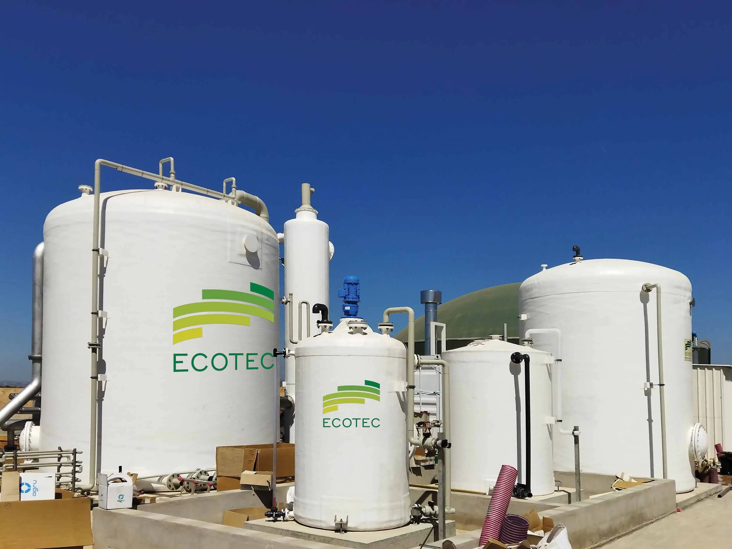 Industrial tanks with piping and machinery at a construction site under a clear blue sky.