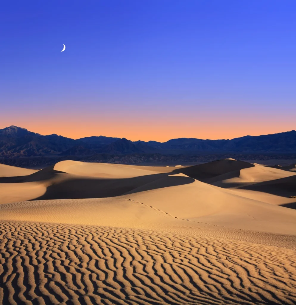 Early Morning Sunlight Merges With A Twilight Moon Over Sand Dunes And Mountains At Death Valley National Park - (PHOTO: DOUG LEMKE/SHUTTERSTOCK)