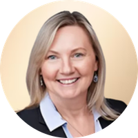 A smiling woman with blonde hair wearing a black blazer and white shirt, posing against a neutral background.