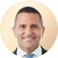 A smiling man with short dark hair, wearing a suit and tie, against a light beige background.