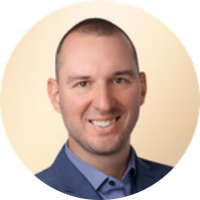 Headshot of a smiling man with short hair, wearing a blue blazer and collared shirt, against a light beige background.