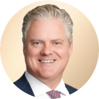 Portrait of a man with gray hair, wearing a suit and tie, smiling against a beige background.
