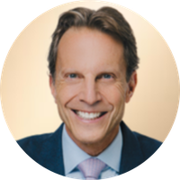 A smiling man with dark hair wearing a suit and tie, against a light-colored background.