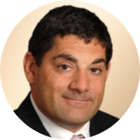 A professional headshot of a man with dark hair, wearing a suit and tie, smiling slightly.