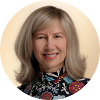 A smiling woman with shoulder-length gray hair, wearing a colorful floral-patterned top, against a neutral background.
