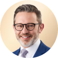 A professional man with glasses, short gray hair, and a beard, smiling in front of a light-colored background.