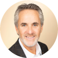 Smiling middle-aged man with gray hair, beard, wearing a dark blazer and white shirt, posing against a beige background.