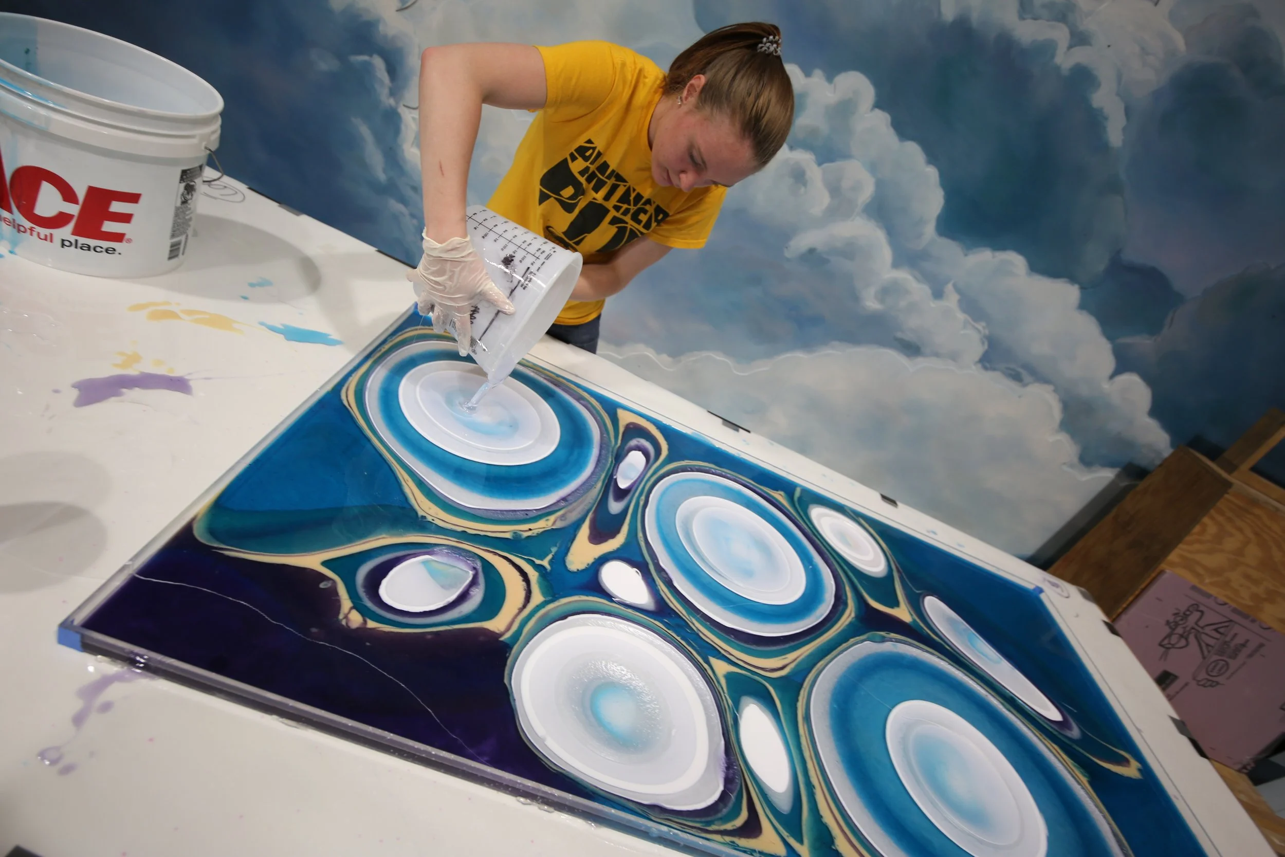Spolar Studio artist pouring epoxy resin to create custom abstract artwork with swirling blue, white, and purple patterns.