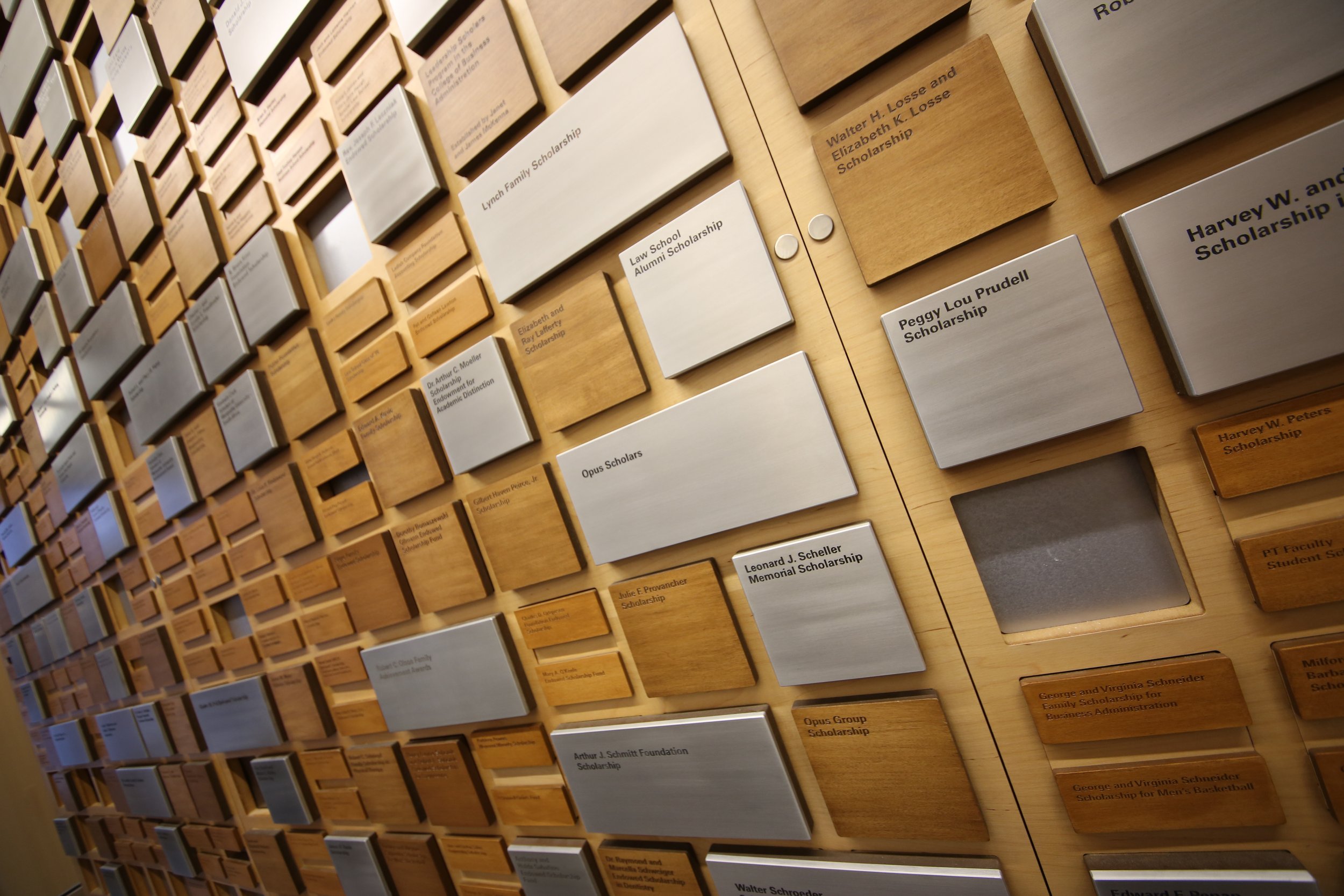 Custom donor recognition installation for a higher education institution featuring dimensional metal plaques, engraved wood panels, and a modular recognition layout.