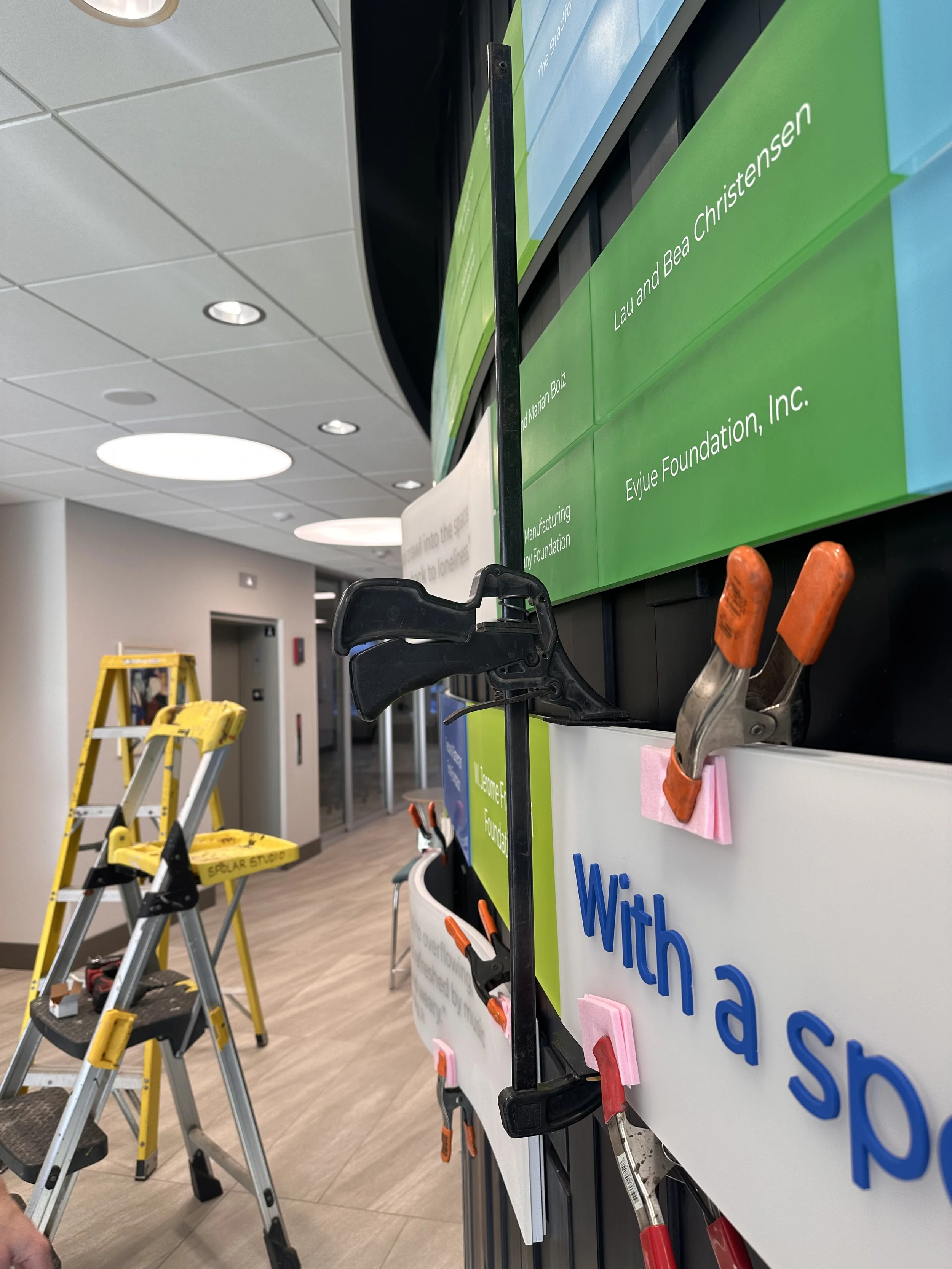 Donor recognition panels being aligned and secured with clamps during on-site installation.
