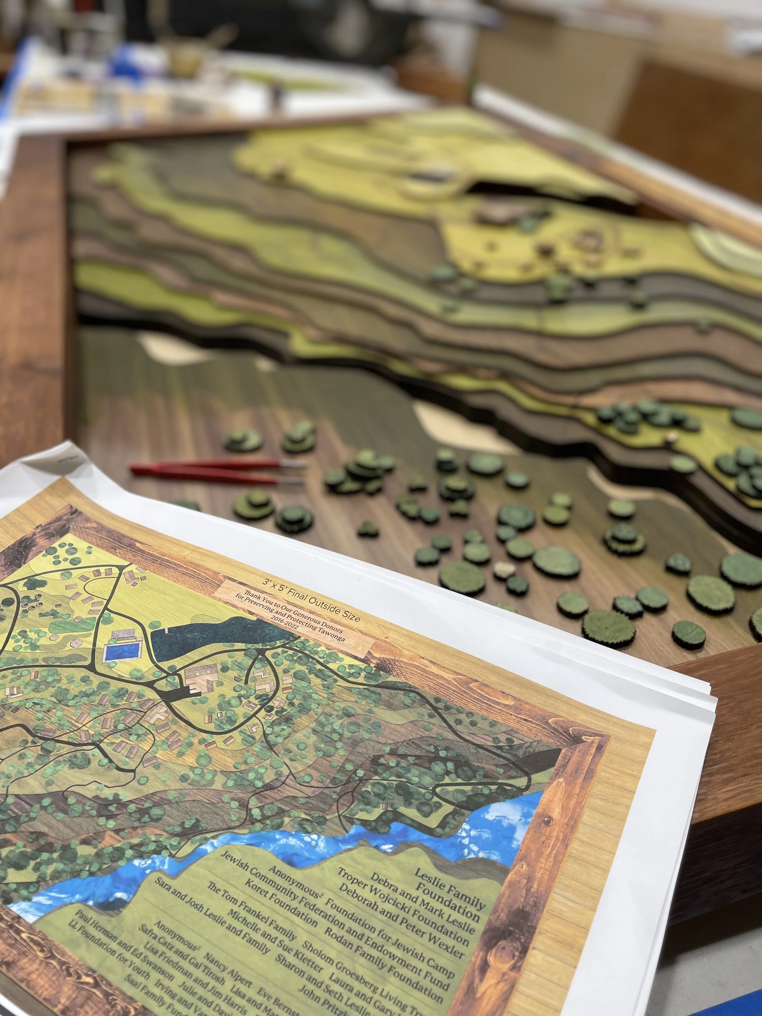 Small fabricated components and layered materials being assembled into a custom display.