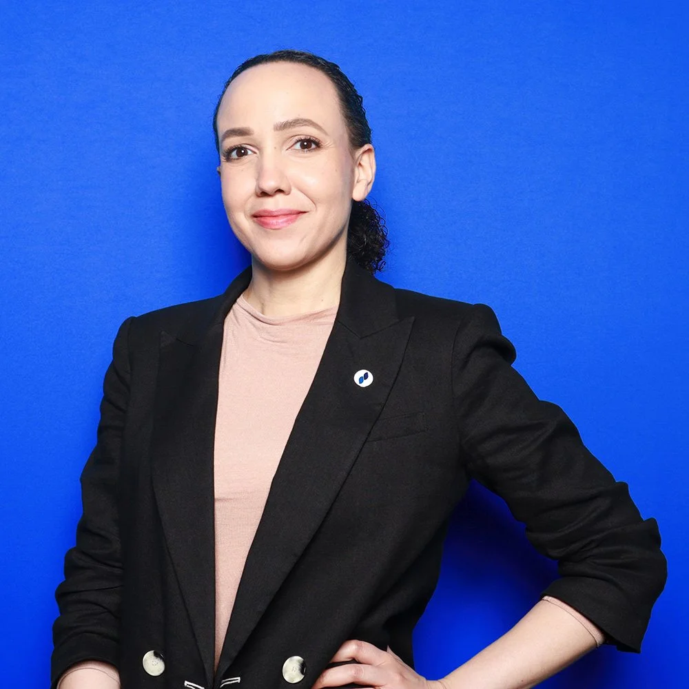 Ashleigh Axios stands, smiling with a Public Servants LLC pin on her blazer lapel