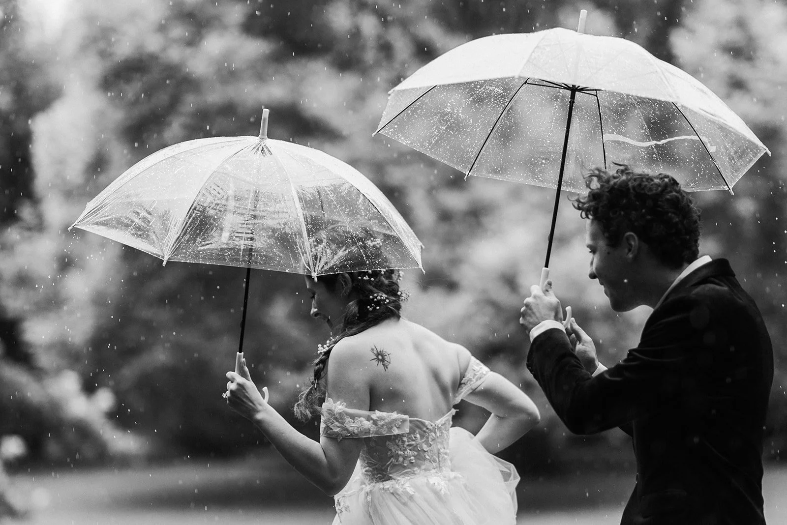 Two Newlyweds running in the rain under umbrellas in Alexandra Gardens, Melbourne, Australia, on their elopement day. Photograph in black and white by Lovelenscapes Photography