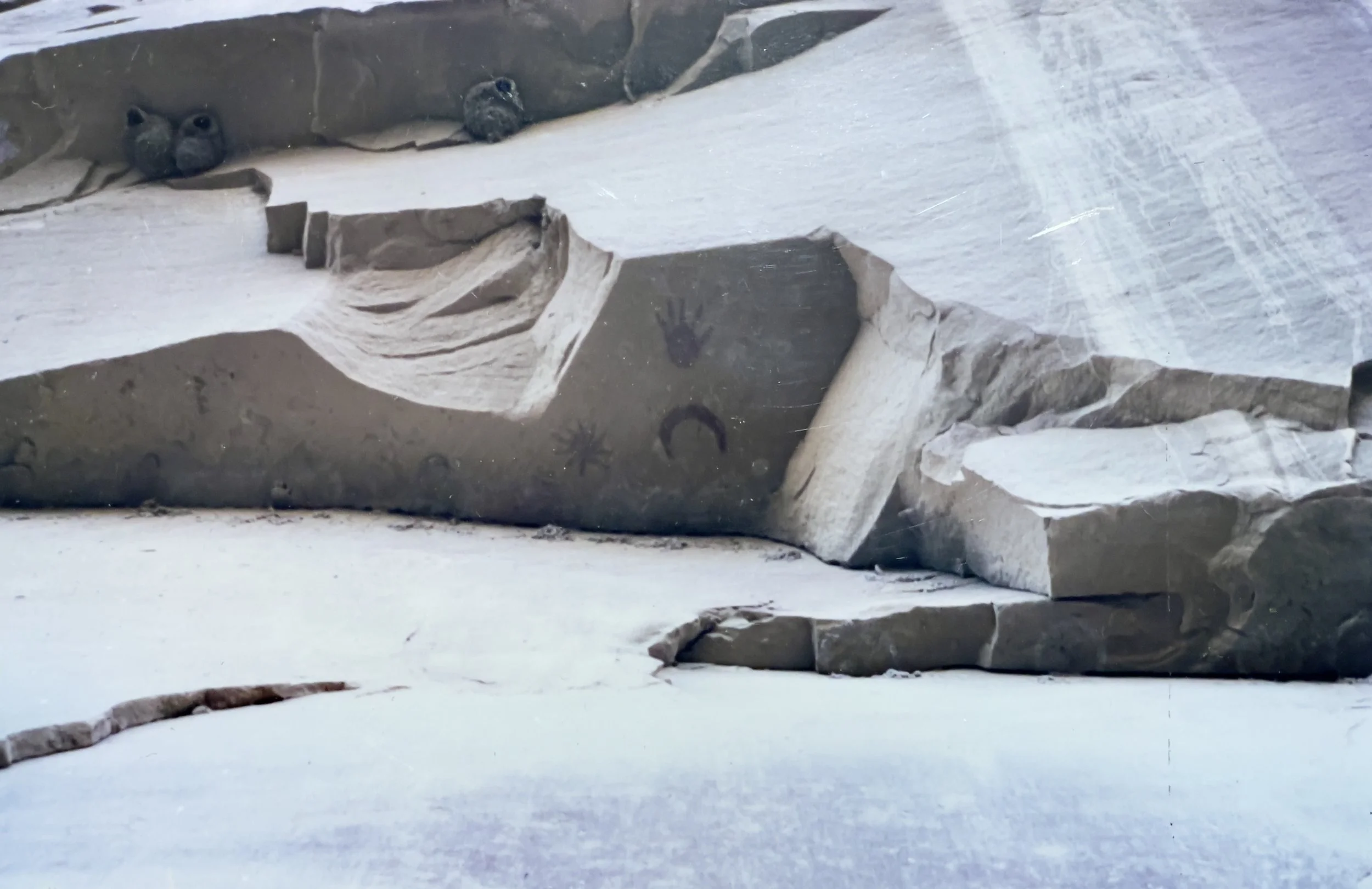 Close-up of a rock formation with carved symbols and a small handprint, surrounded by snow.
