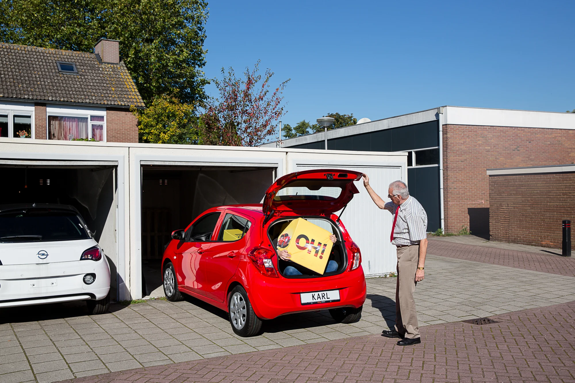 Verkoopadviseur Tim van Arent in de nieuwe Opel Karl bij Orange Motors in Berkel en Rodenrijs. Ook op de foto: buurtbewoner Theo de Bruin.
