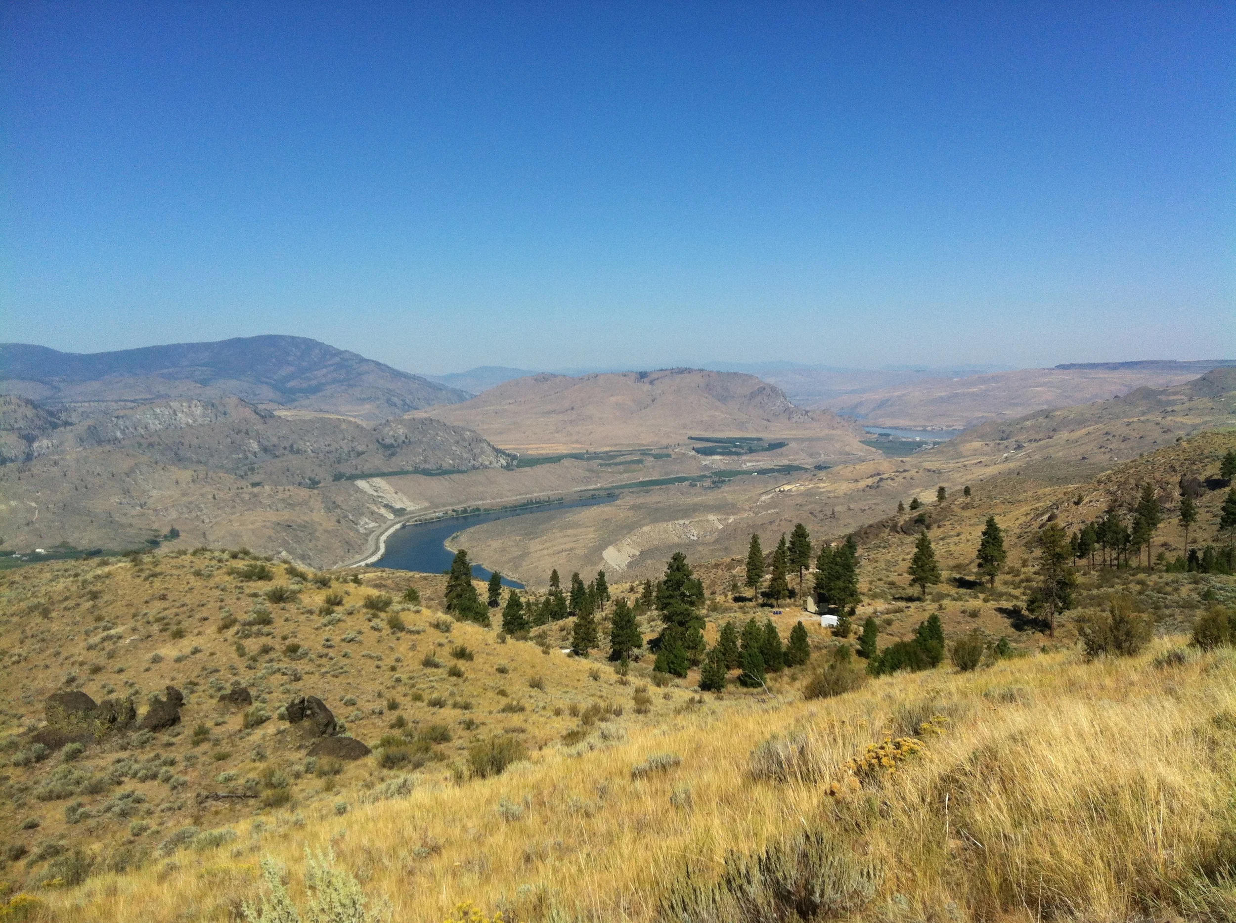 Looking North along the Columbia. Without the haze, Canadian peaks are visible in the distance. Road J serves the rest of the small tree-dotted plateau below where you can see a few more small structures.