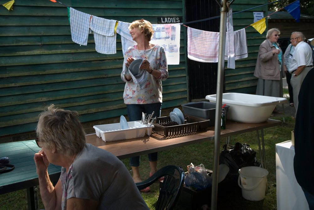 Copy of Ebernoe Horn Fair West Sussex, UK 2015. Tea tent lady washing and drying dishes.