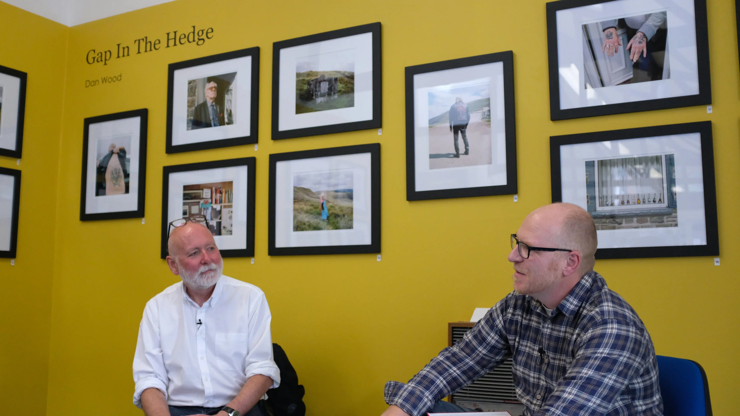 Paul Cabuts and Dan Wood in conversation - with a selection of work from ‘Gap in the Hedge’ on the walls around them.