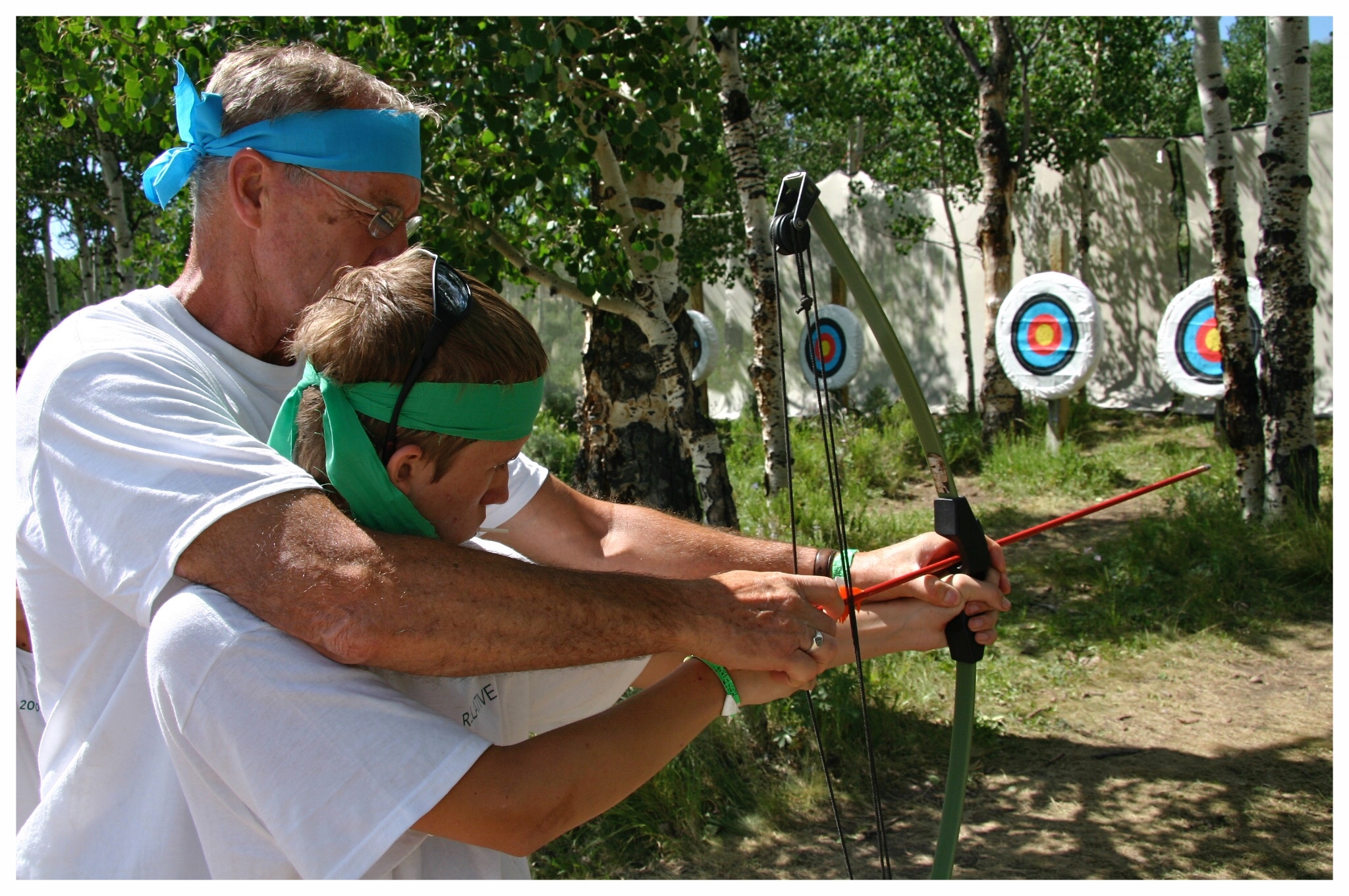 Taken at a family reunion in 2009. We split up into teams, designated by the color of our headbands, for some fun competition. Grandpa is giving Chase some archery tips!