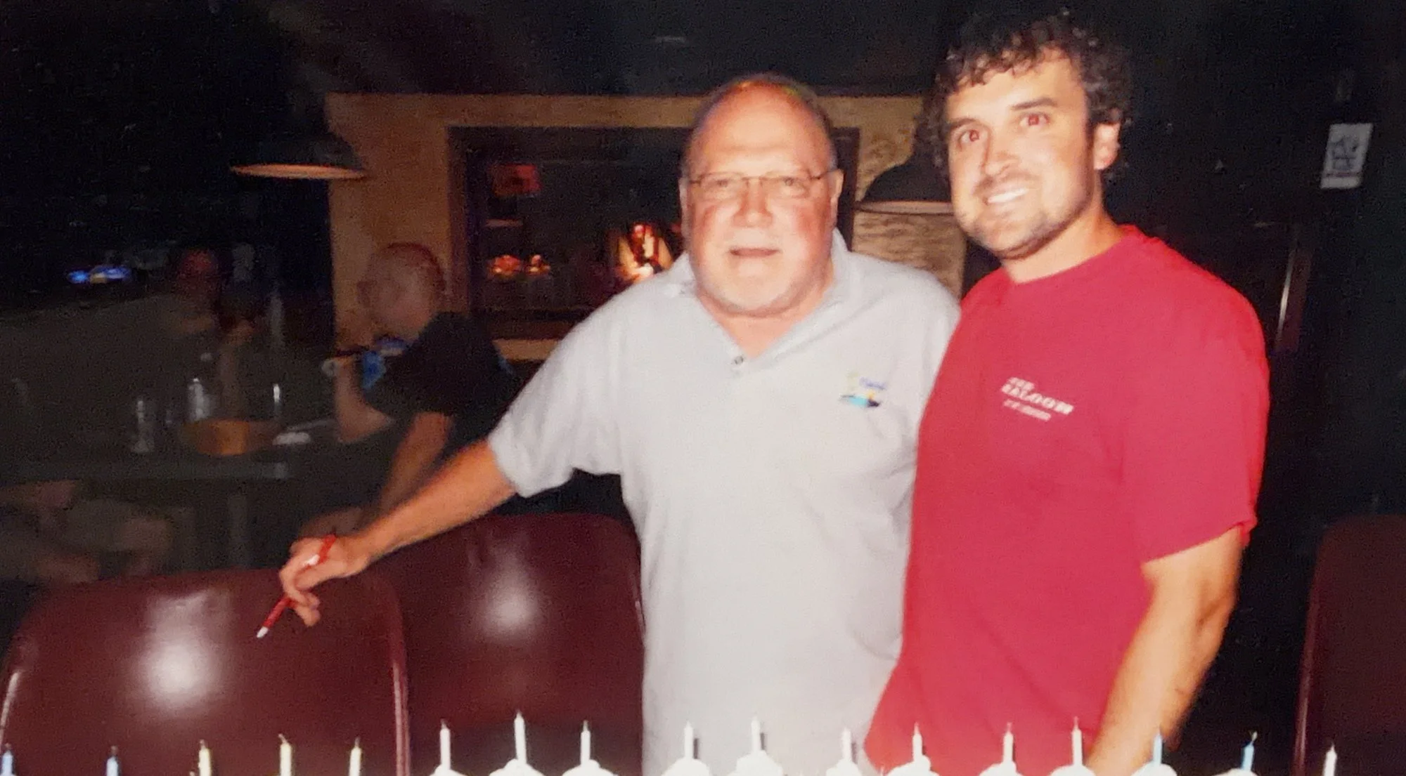 Saloon founder Jim Sheppard and Keith Sheppard at the bar, smiling over anniversary cake candles