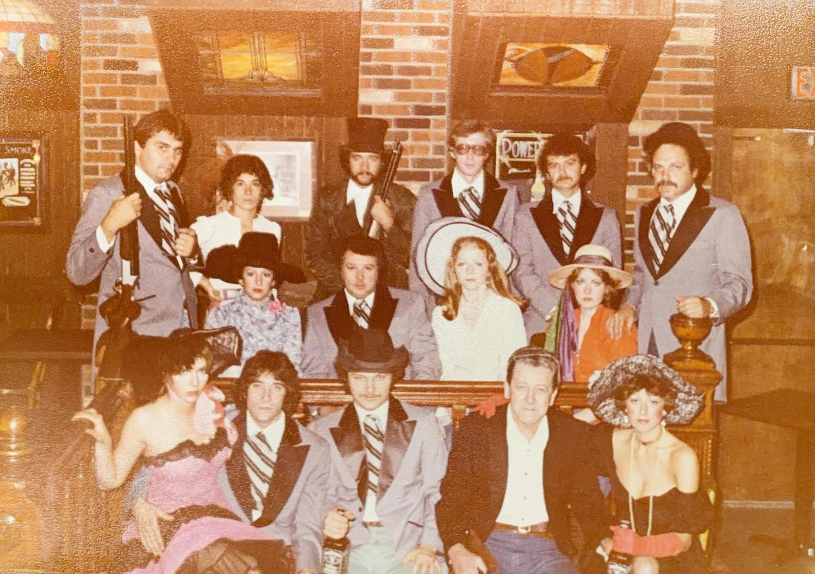 The Saloon's original 1976 staff in Old West costume, posed in front of the brick wall and stained-glass windows