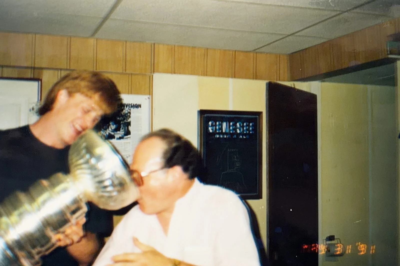 Saloon founder Jim Sheppard drinks from the Stanley Cup in the bar's back office while Penguin Troy Loney holds it, May 31, 1991