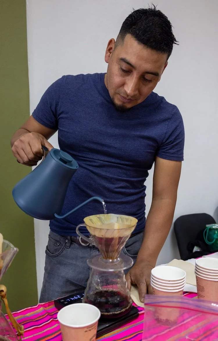 Person brewing pour over coffee by slowly pouring hot water through a filter into a glass carafe