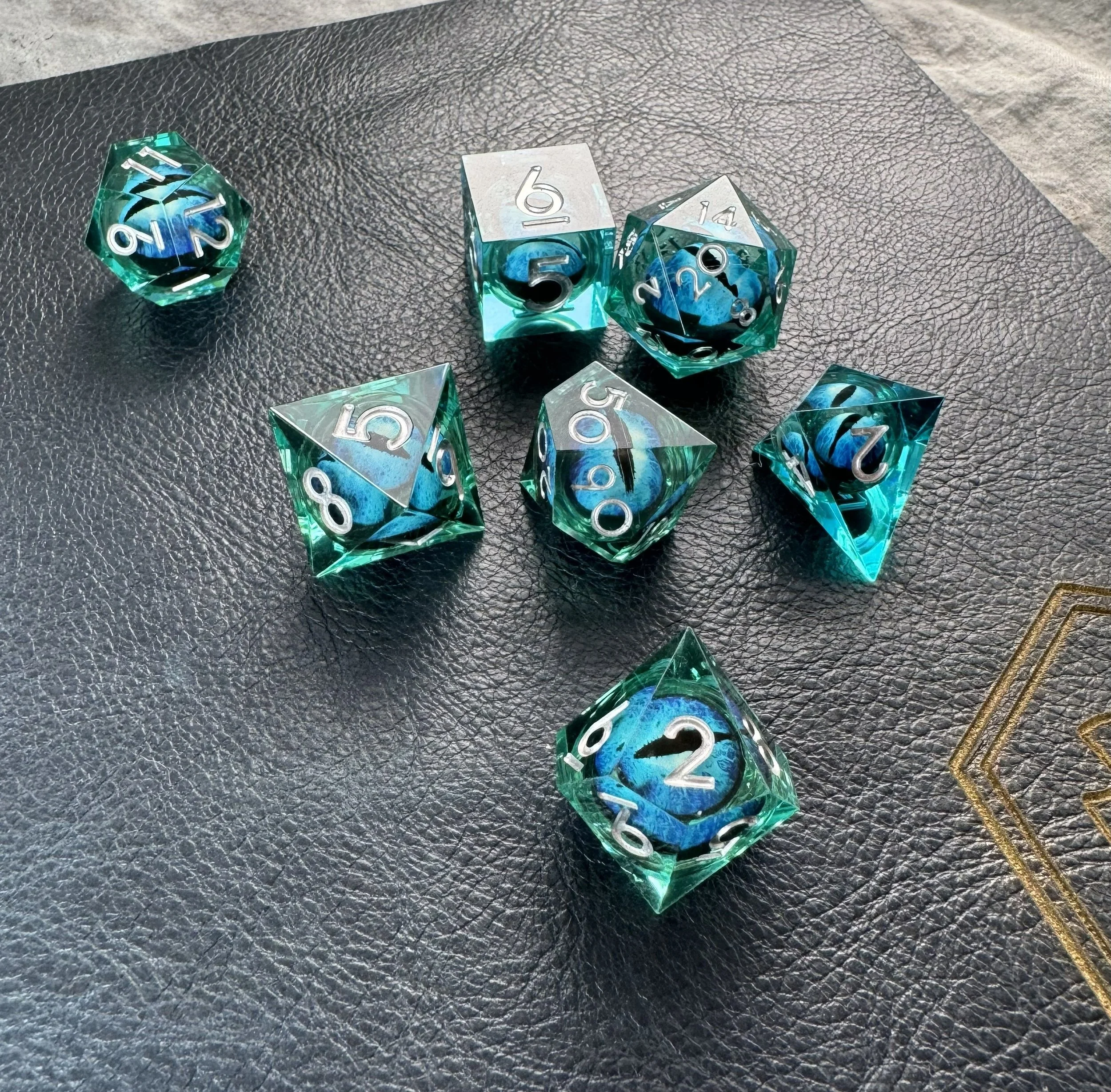 Close-up of a 7-piece sharp edge polyhedral dice set with a floating blue and black dragon eye core suspended in blue resin sitting on a blue leather play mat