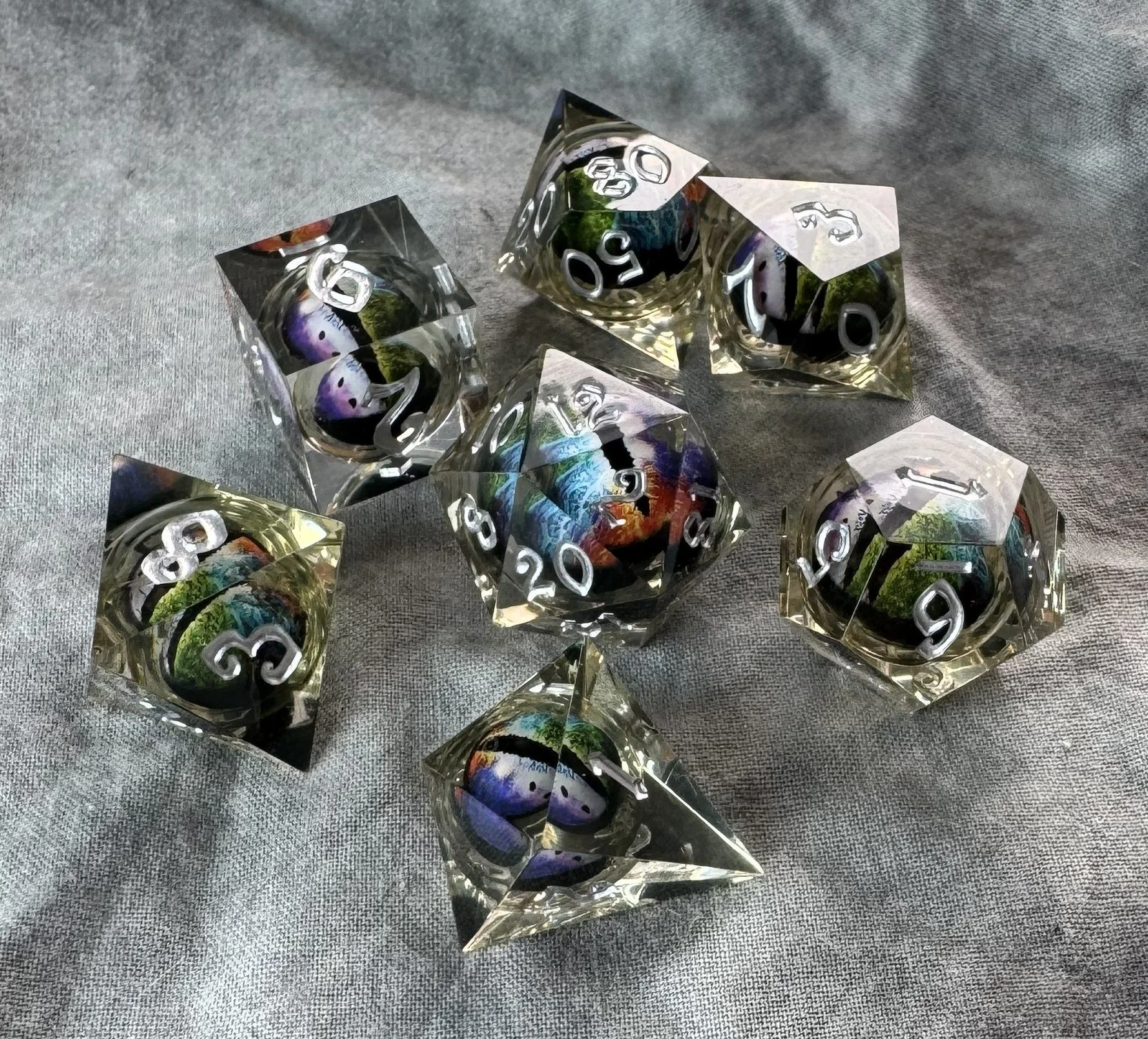 A 7-piece sharp edge polyhedral dice set with a floating multicolor rainbow dragon eye core suspended in crystal clear resin.