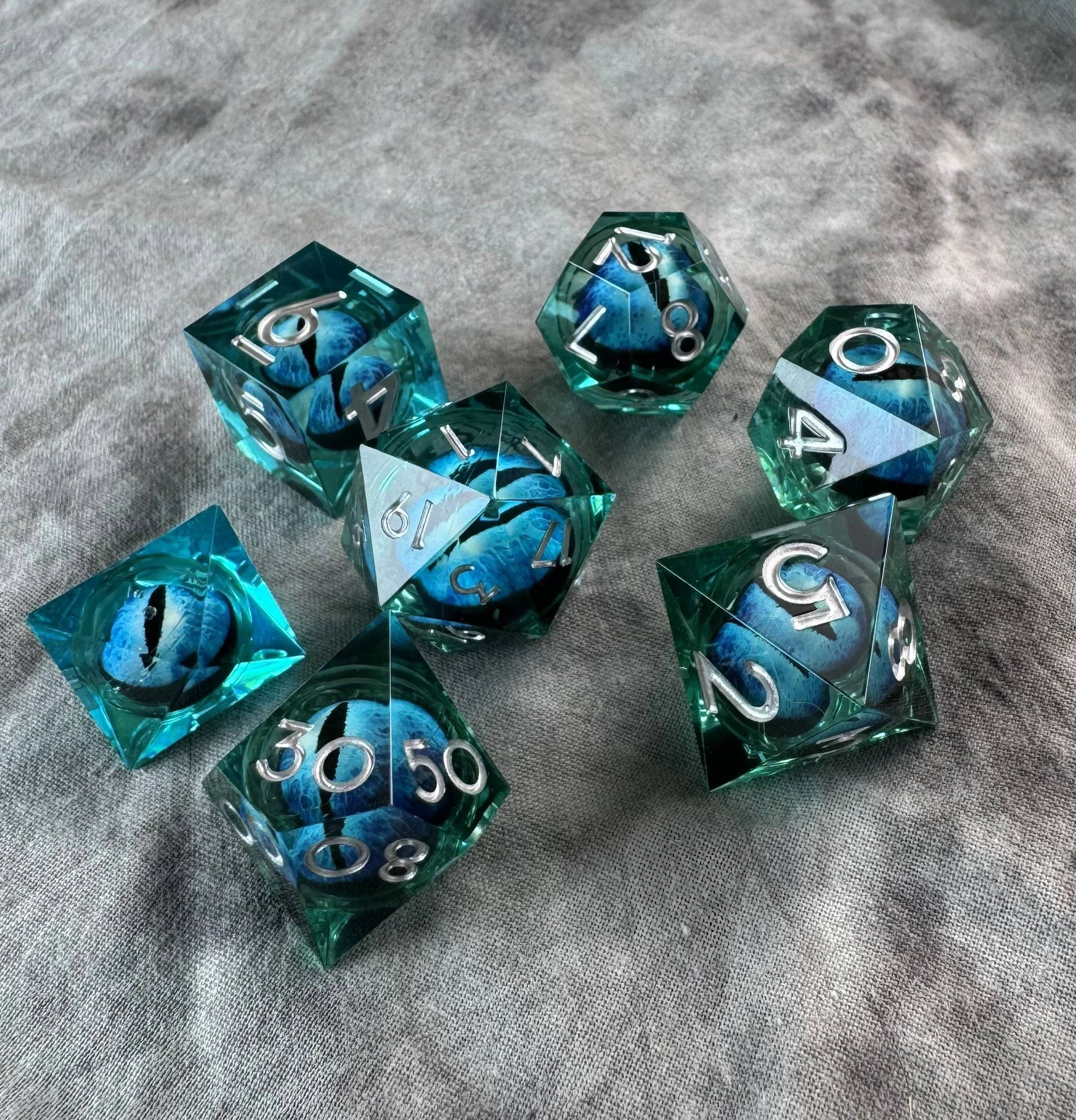 Close-up of a 7-piece sharp edge polyhedral dice set with a floating blue and black dragon eye core suspended in blue resin