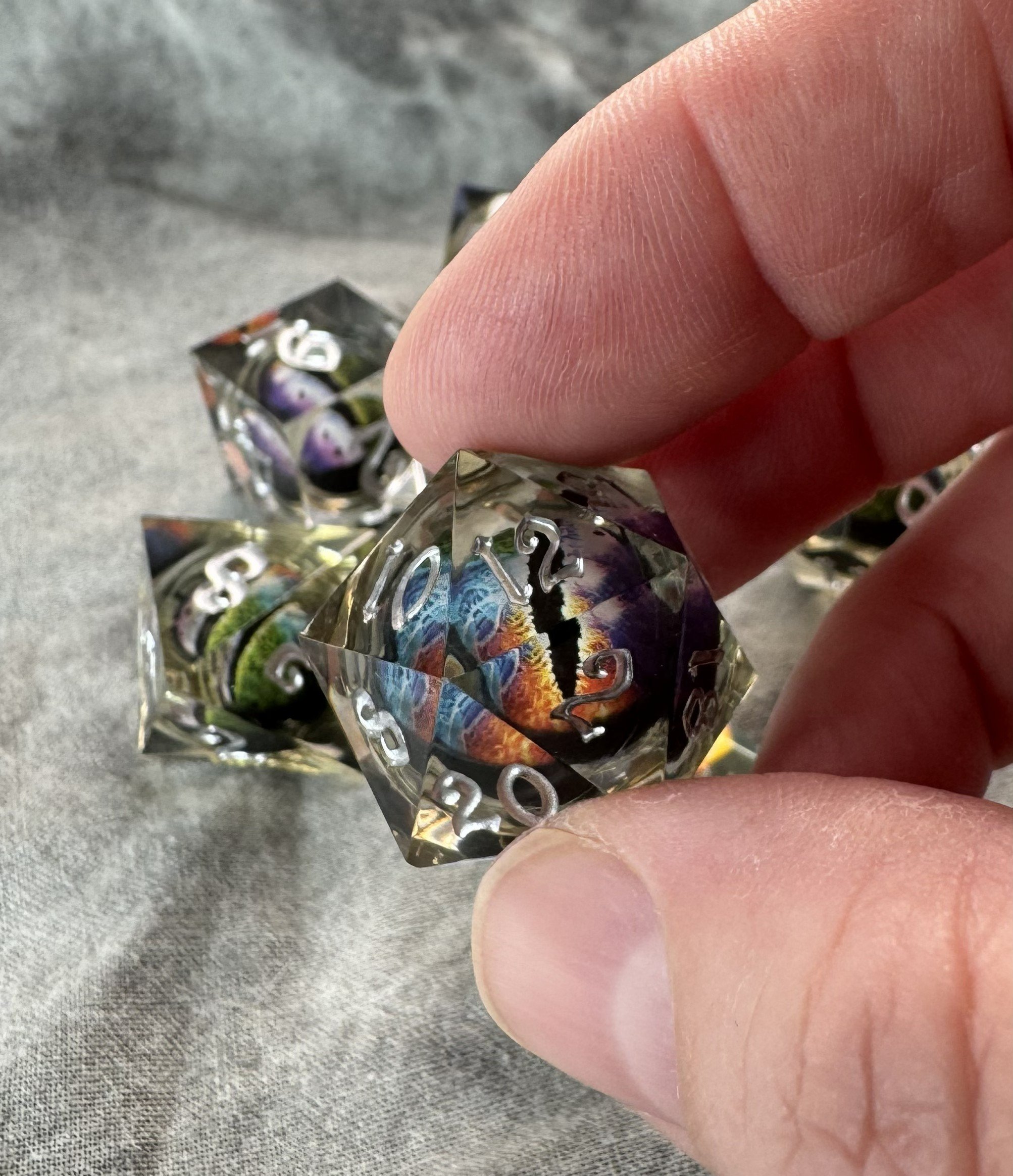 Close-up of a 7-piece sharp edge polyhedral dice set with a floating multicolor rainbow dragon eye core suspended in crystal clear resin