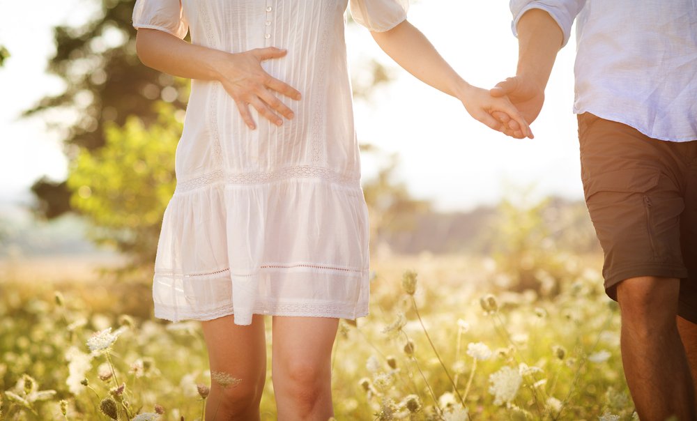happy young pregnant couple walking in field - shutterstock_150045185.jpg
