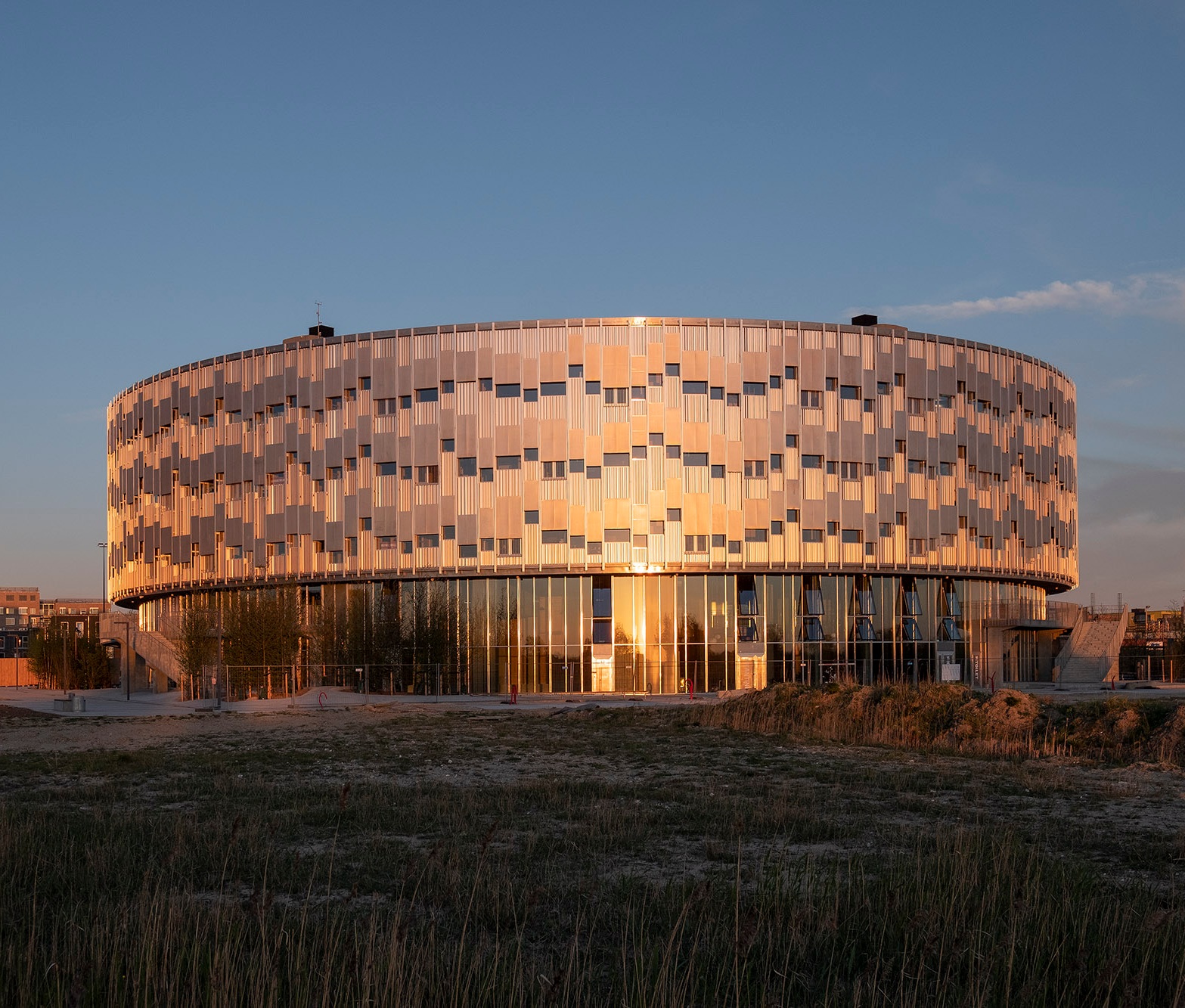 Den lette, højisolerede aluminumsfacade fordeler sig rytmisk i et lys- og skyggespil mellem lukkede, åbne og perforerede felter, der både sikrer afskærmning mod solen og udsyn.