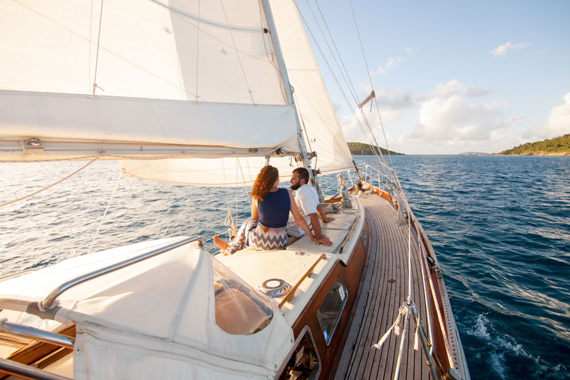 A couple is seated on the bow of a sailboat, celebrating their engagement with Cimarron Yacht Charter in  the crystal clear waters of St. John.