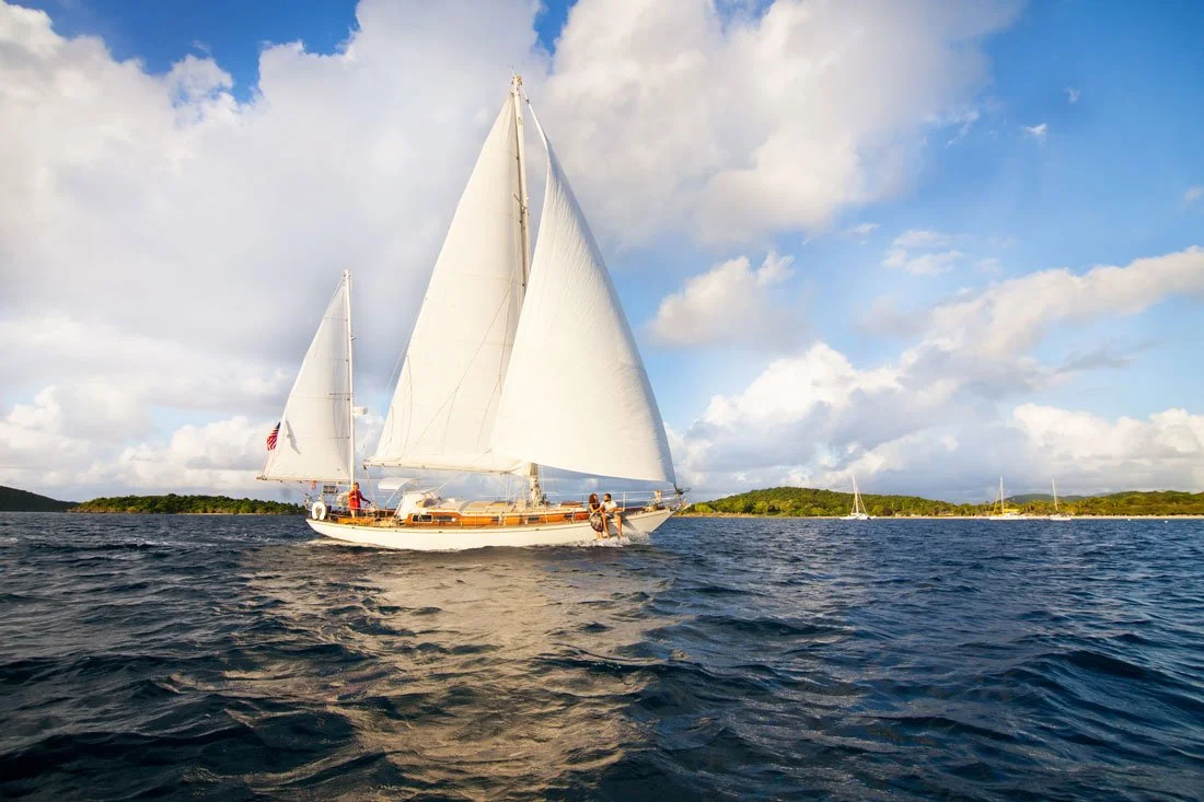 A beautiful Cimarron Yacht Charter wooden sailboat with grand white sails, glides through the Caribbean Sea, in St John, USVI.