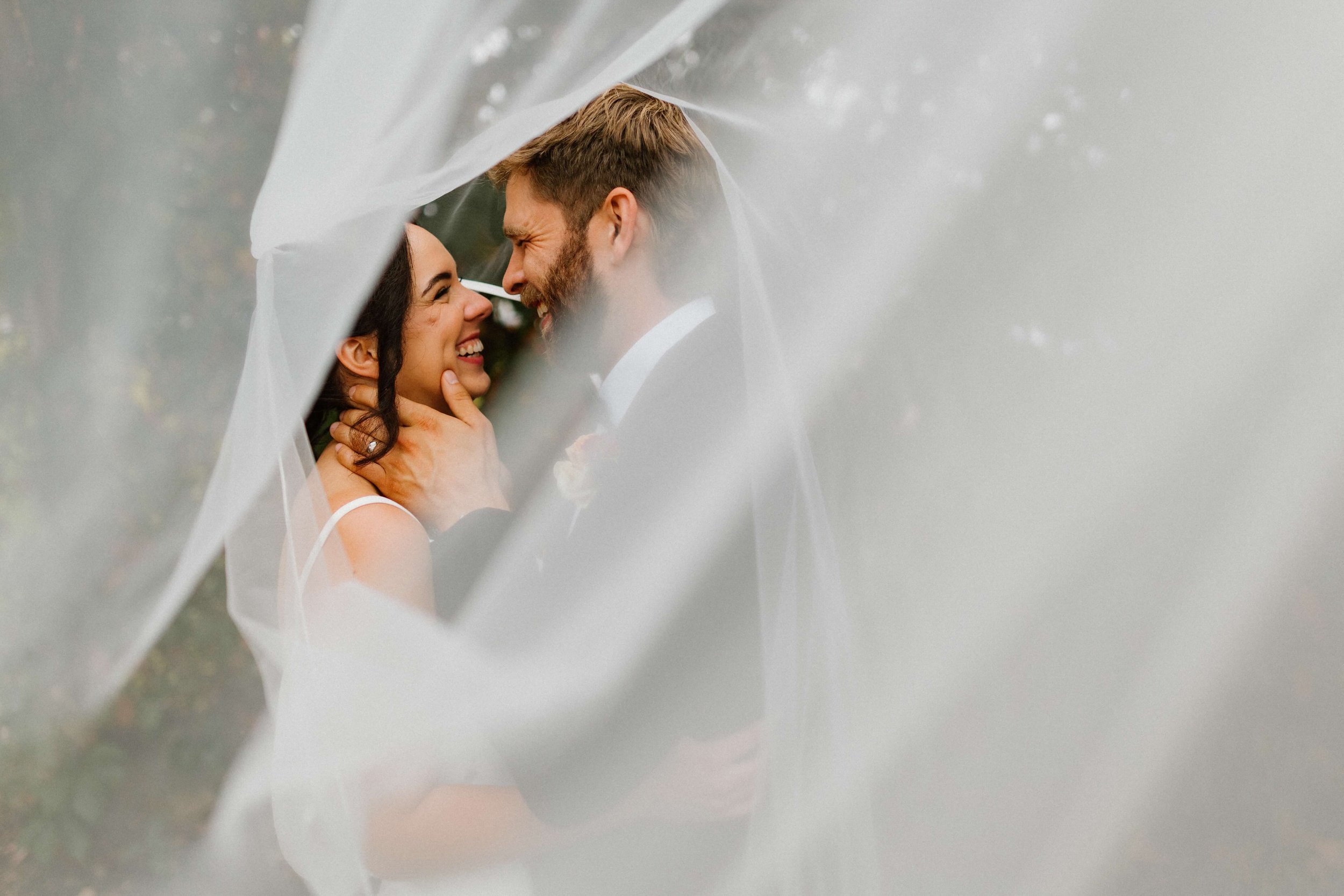 Couple laughing together wrapped in wedding veil.jpg