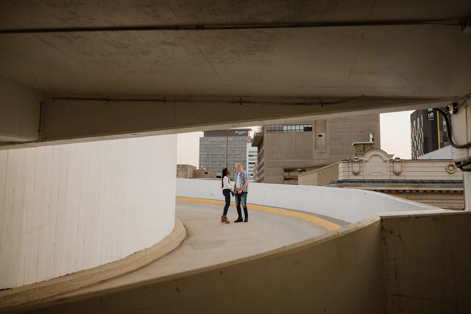  Couple standing together on a curved parking garage ramp during an urban engagement session in Winnipeg 