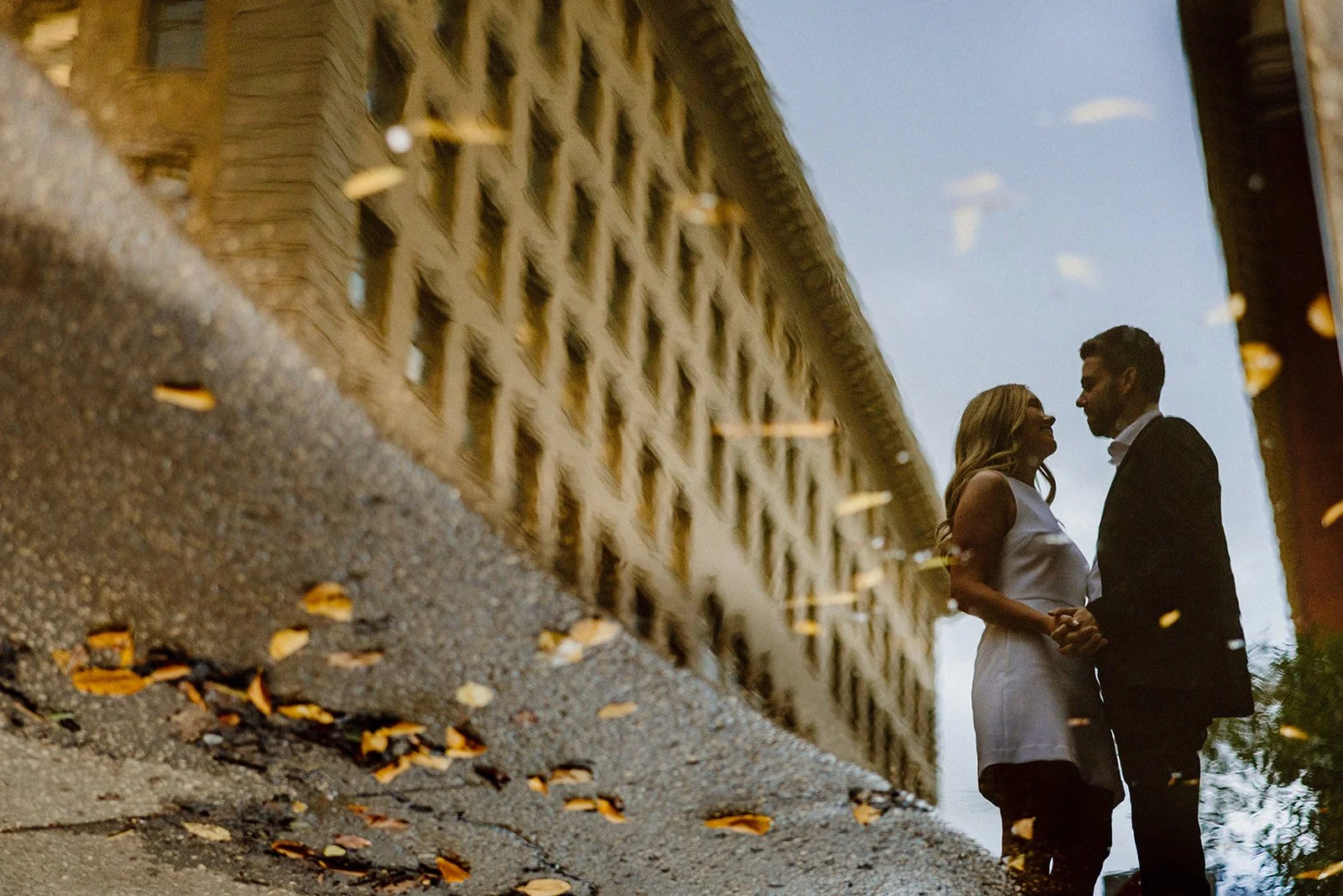  Couple standing together reflected in a puddle in the Exchange District during an engagement session in Winnipeg 