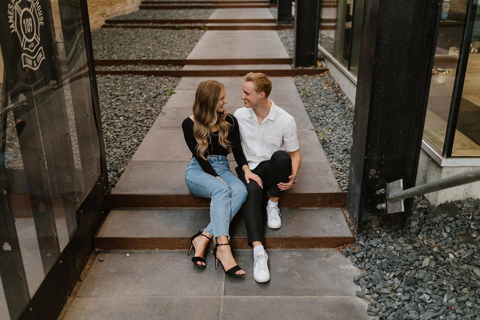  Couple sitting together on concrete steps along the waterfront during an engagement session in Winnipeg 