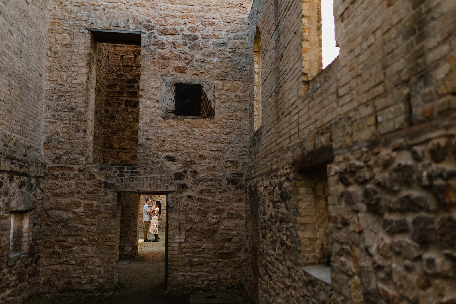  Couple standing together in a stone archway at the St Norbert Monastery Ruins during an engagement session in Winnipeg 