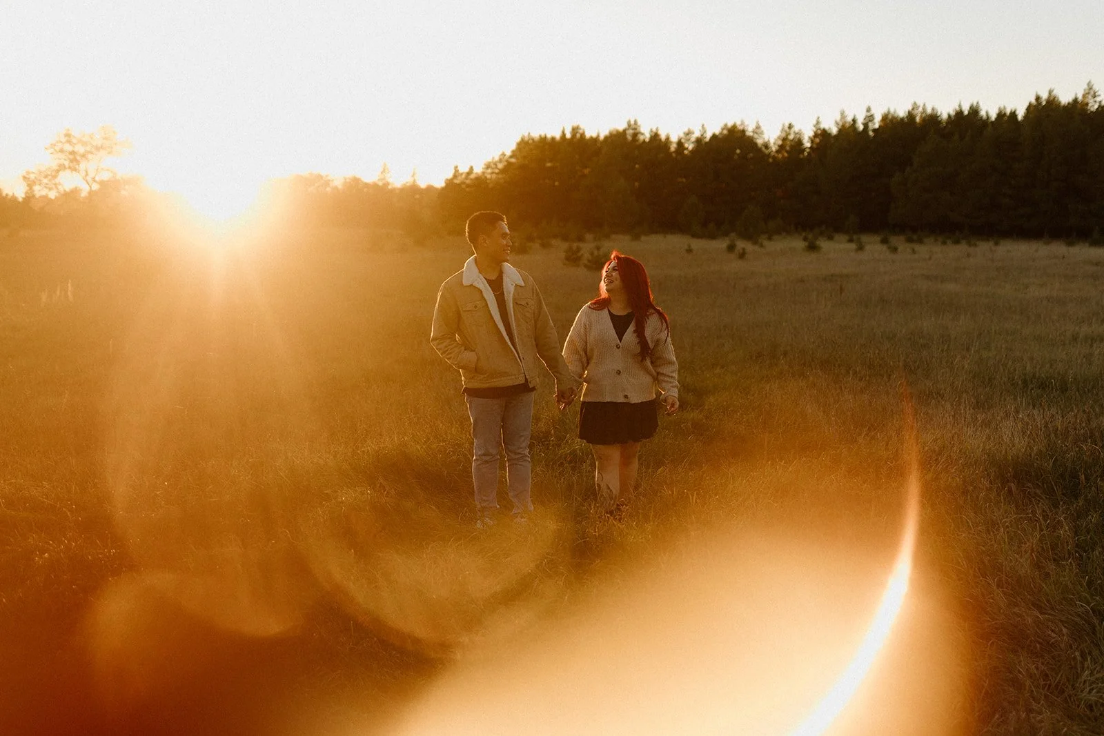  Couple walking through a golden field at sunset in Birds Hill Park near Winnipeg with warm lens flare 