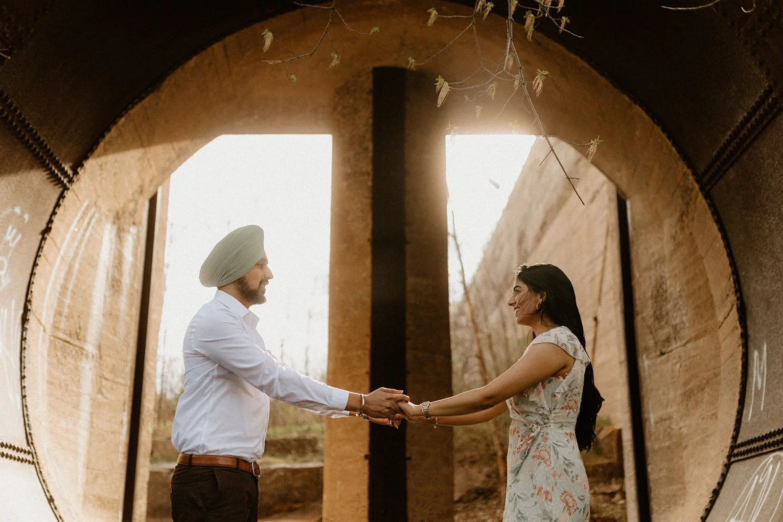  Couple holding hands under a stone archway at Pinawa Dam in Manitoba, backlit by warm sunset light through historic ruins 