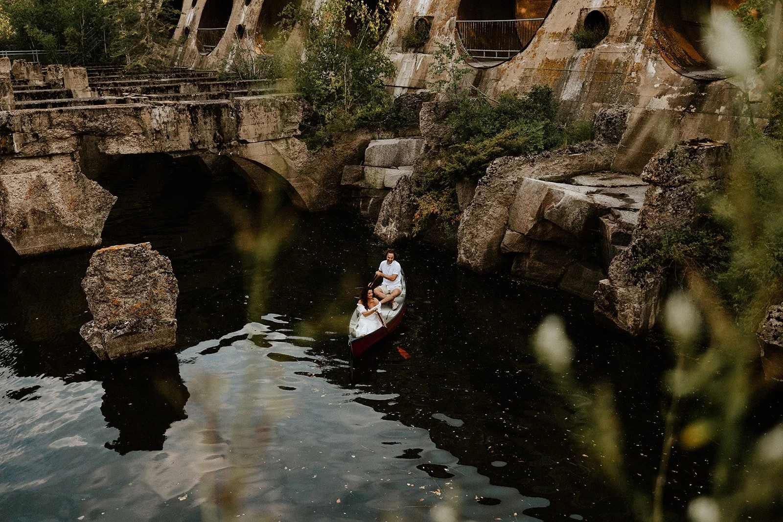  Couple in a canoe beneath the historic Pinawa Dam ruins in Manitoba, surrounded by stone structures and calm river water 