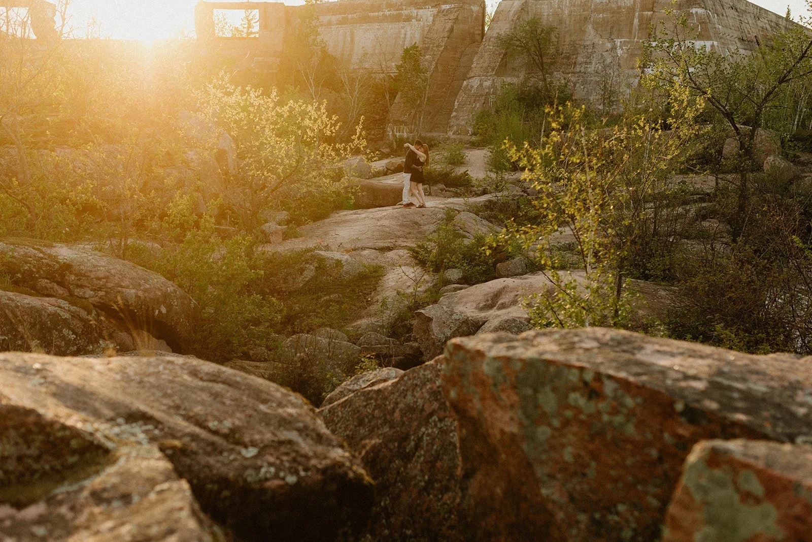  Couple standing on rocky terrain at Pinawa Dam in Manitoba during sunset, surrounded by warm light and natural landscape 