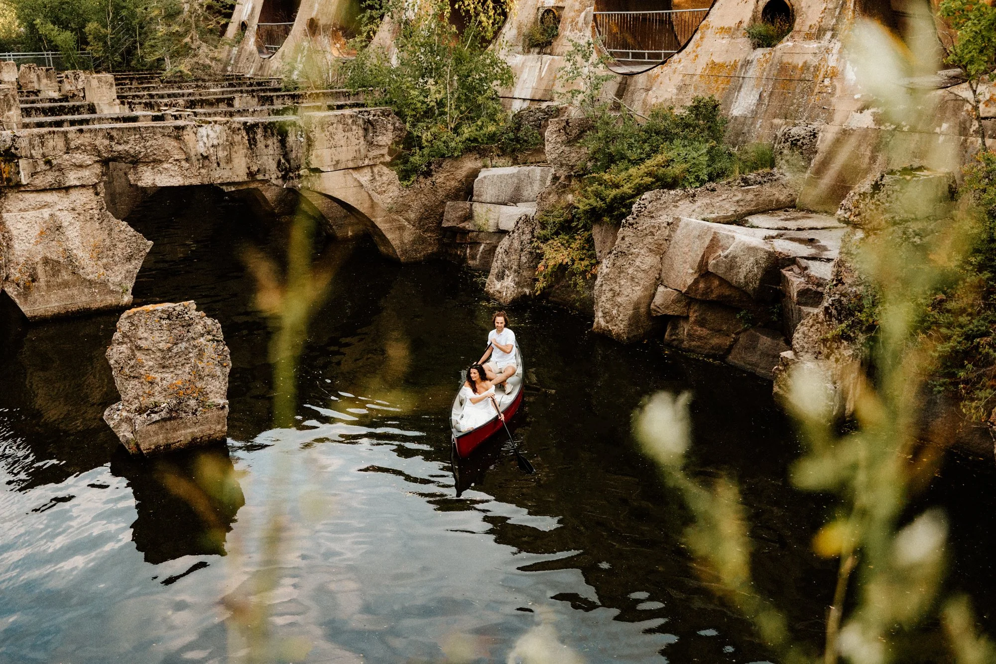  Couple in a canoe beneath the historic Pinawa Dam ruins in Manitoba, surrounded by stone structures and calm river water 