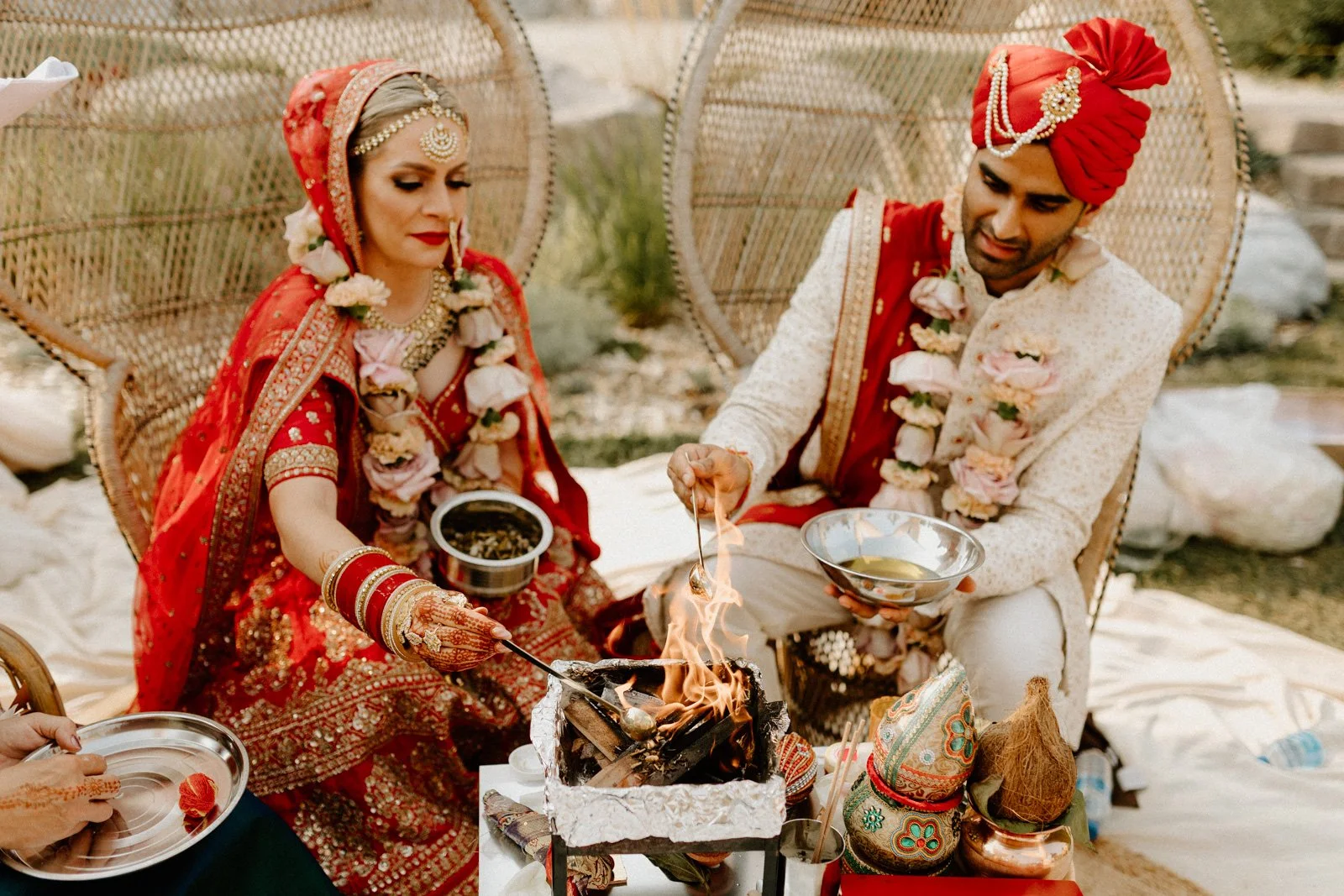 Bride and groom performing a Hindu wedding fire ritual at Hawthorn Estates in Winnipeg, wearing traditional red and cream outfits with floral garlands during the ceremony